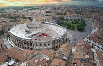 Betagende panoramaudsigt over Verona ved solnedgang med den ikoniske Arena di Verona i centrum og byens historiske arkitektur langs Adige-floden