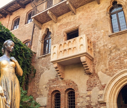 Den berømte bronzestatue af Julie og den ikoniske balkon ved Casa di Giulietta i Verona, Italien, et populært turistmål inspireret af Shakespeares Romeo og Julie, selvom det er en romantisk fantasi