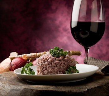 Traditionel risotto all'Amarone fra Verona serveret med et glas rødvin på et rustikt træbord - en smagfuld specialitet fra det lokale køkken