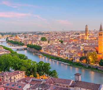 Malerisk udsigt over Veronas historiske skyline ved solnedgang med den snoende Adige-flod og byens ikoniske tårne i romantisk aftenbelysning