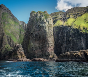 Imponerende Vestmannabjergene på Færøerne med stejle klipper der rejser sig fra det blå hav omgivet af grønne landskaber