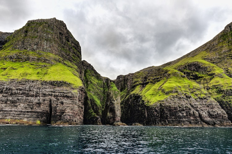 Imponerende udsigt over Vestmanna klipperne på Færøerne med stejle klipper der rejser sig fra det turkisblå hav under en solrig himmel