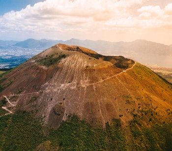 Luftfoto af vulkanen Vesuv nær Napoli i Italien med det karakteristiske krater og grønne omgivelser under blå himmel