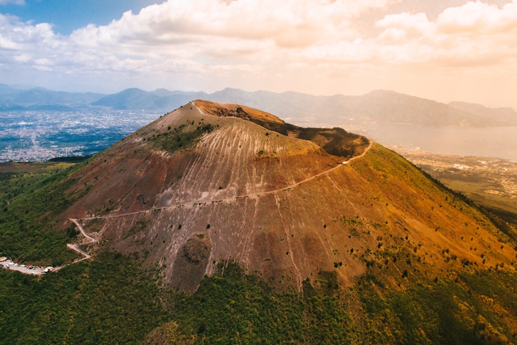 Luftfoto af vulkanen Vesuv nær Napoli i Italien med det karakteristiske krater og grønne omgivelser under blå himmel