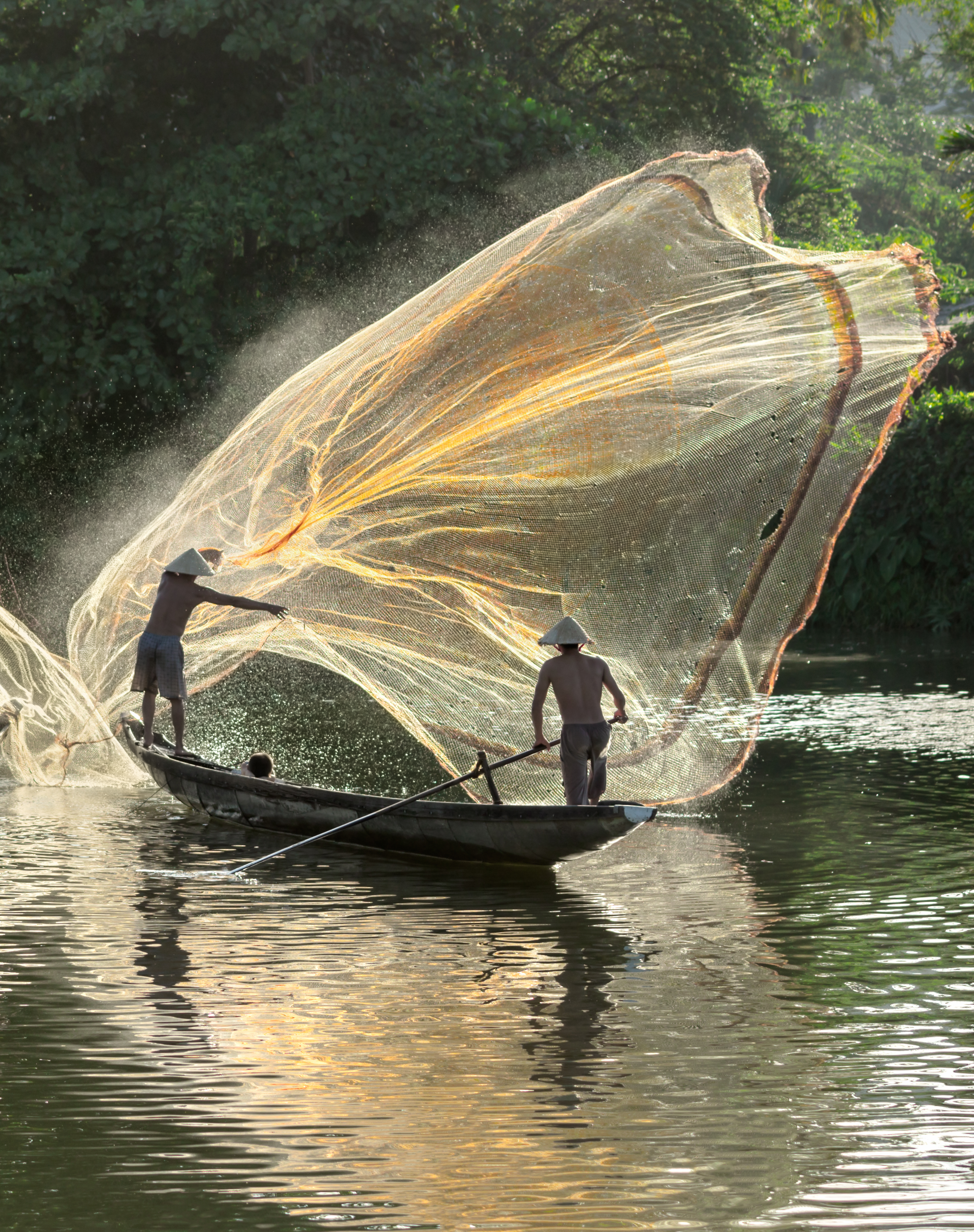 Traditionelle vietnamesiske fiskere kaster net fra træbåd ved solopgang på flod