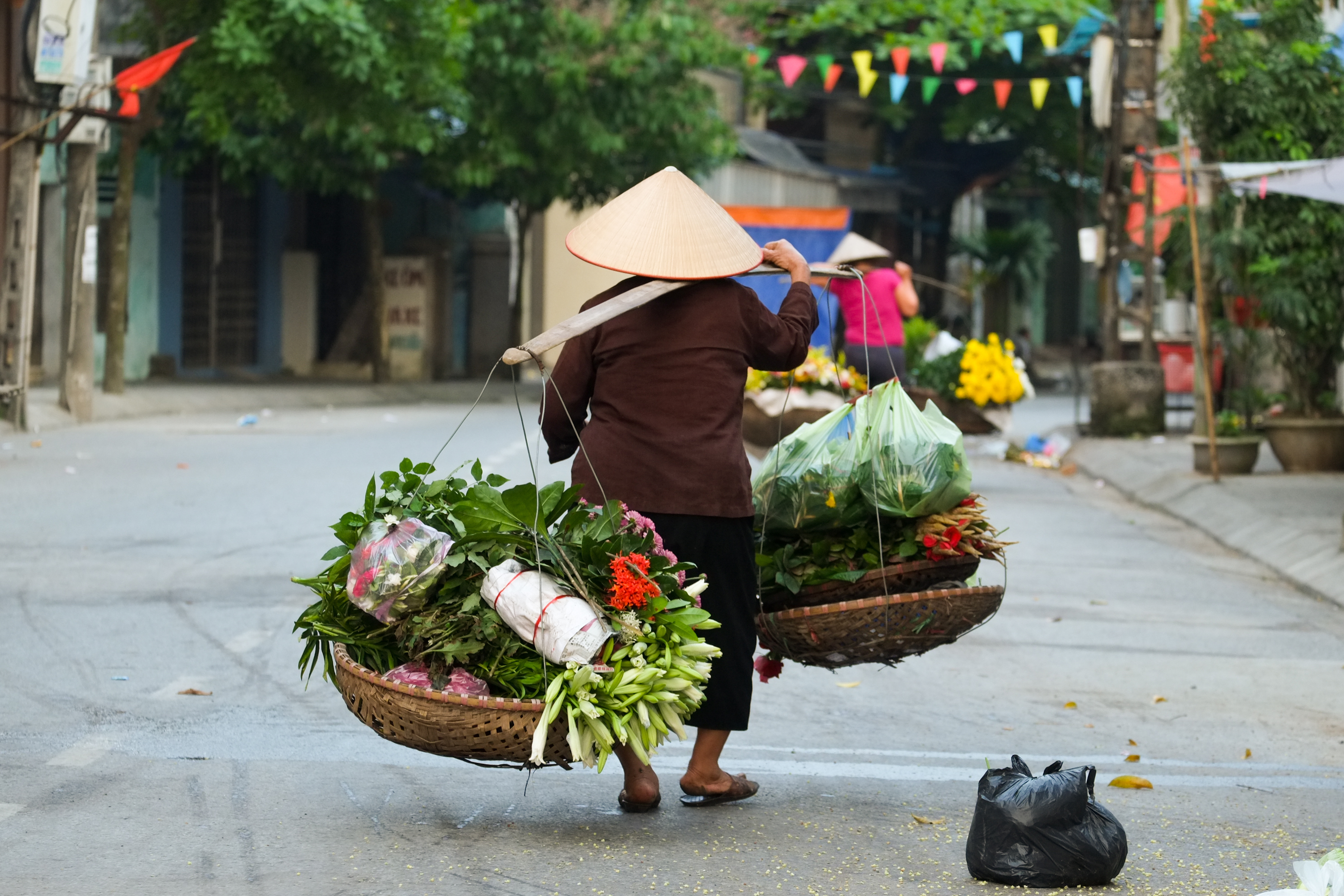 Vietnamesisk gadesælger med traditionelle kurve fyldt med friske blomster i Hanoi