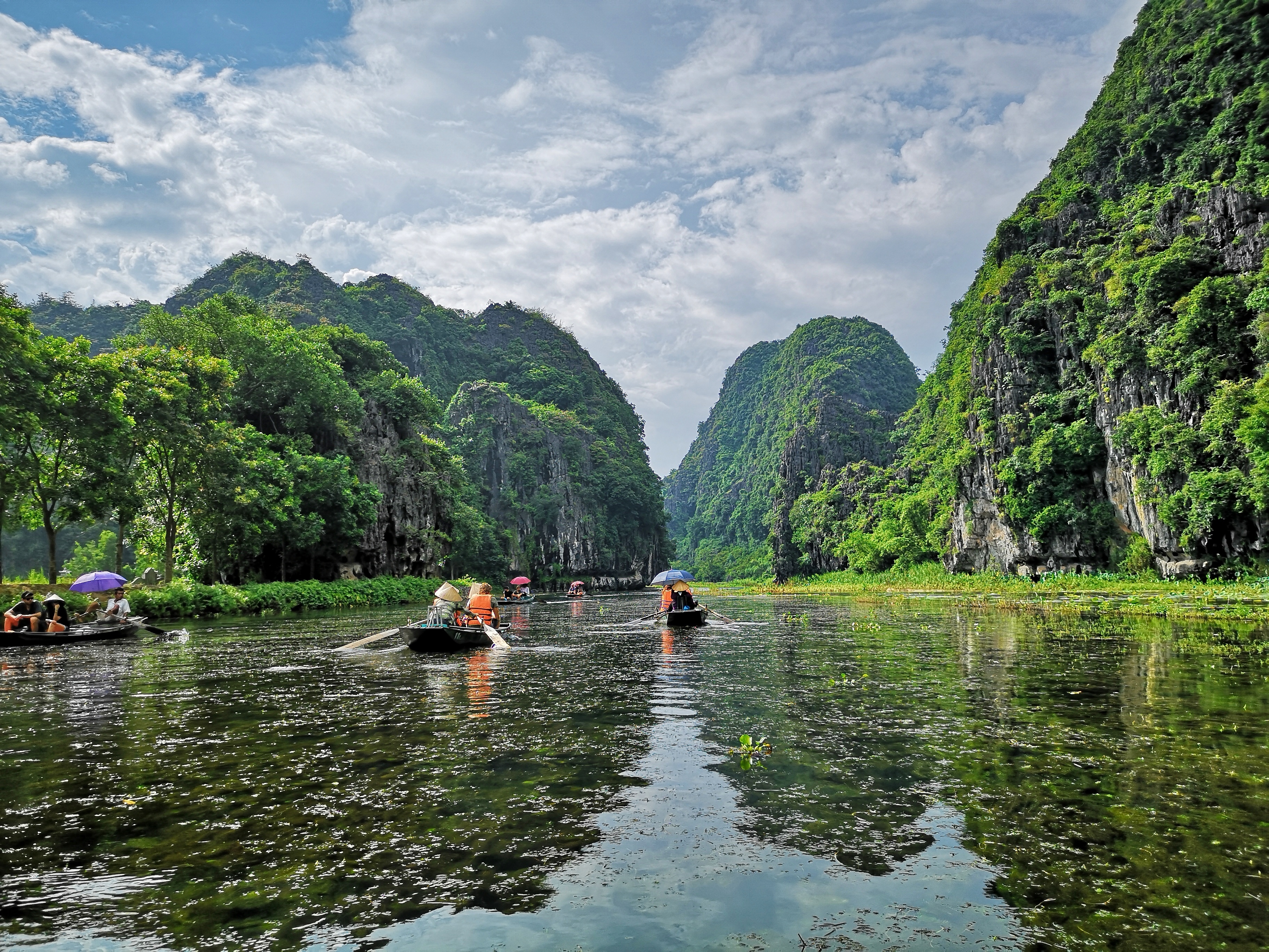 Traditionelle både sejler mellem kalkstensklipper i Ninh Binh Vietnam med turister på flodcruise