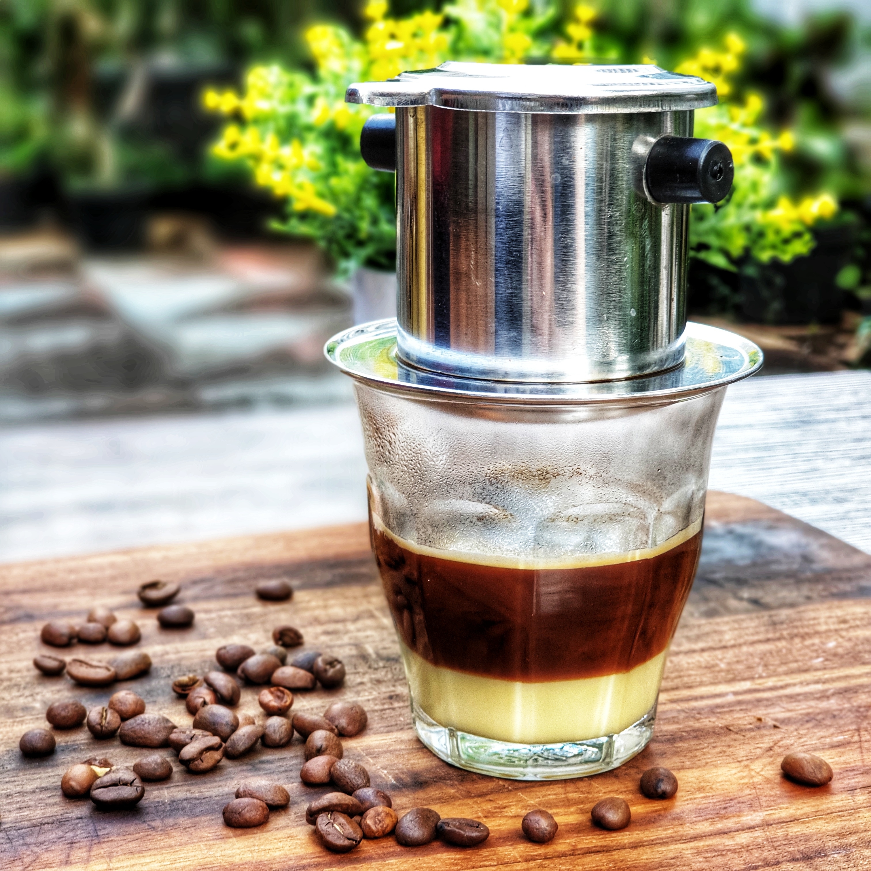 Traditionel vietnamesisk drypkaffe brygget i et phin-filter over et glas med kondenseret mælk på et træbord i Vietnam