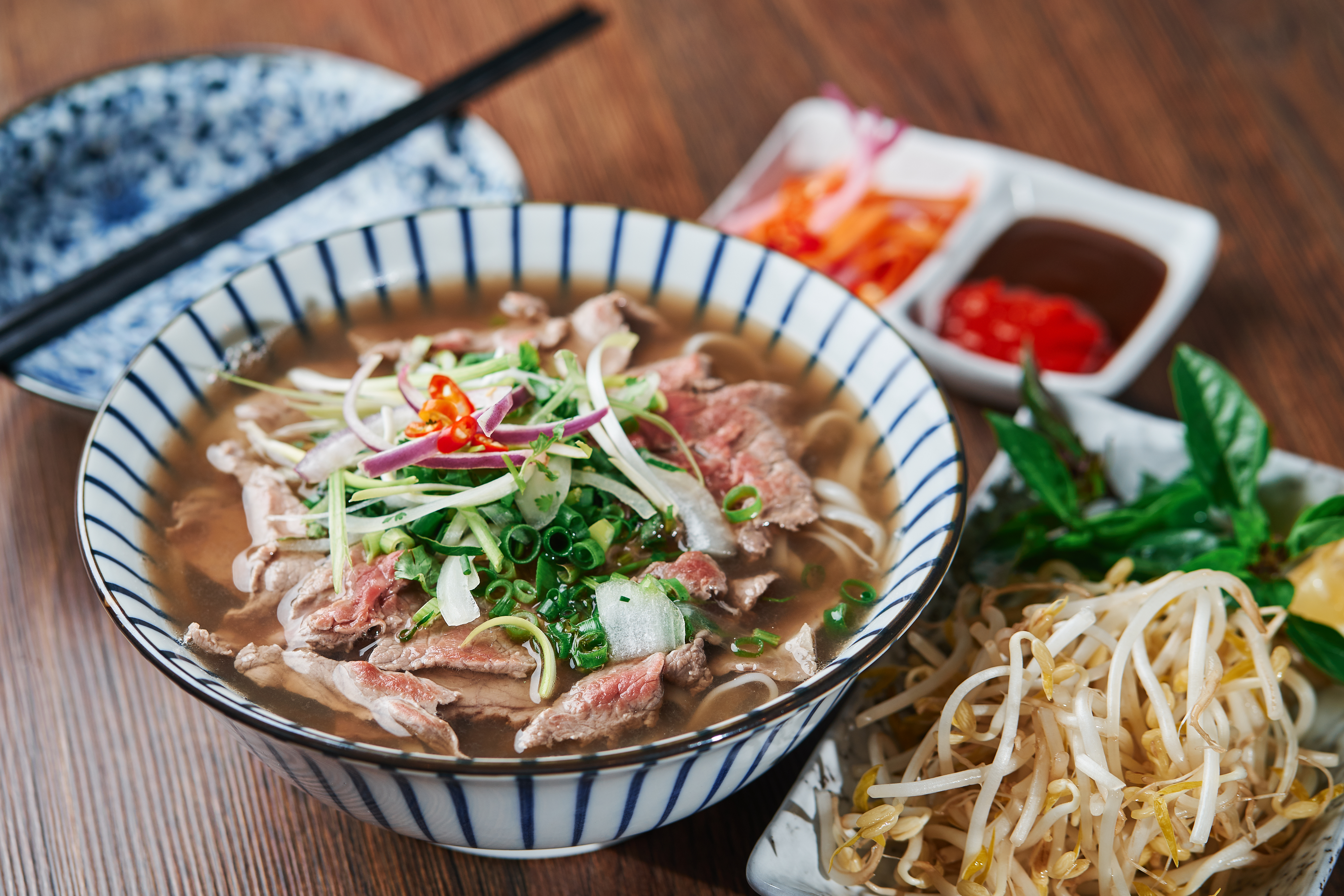 Traditionel vietnamesisk Pho Bo oksekødsnudlesuppe serveret i skål med friske krydderurter, bønnespirer og chilipepper i Vietnam
