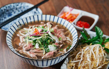 Traditionel vietnamesisk Pho Bo oksekødsnudlesuppe serveret i skål med friske krydderurter, bønnespirer og chilipepper i Vietnam