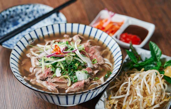 Traditionel vietnamesisk Pho Bo oksekødsnudlesuppe serveret i skål med friske krydderurter, bønnespirer og chilipepper i Vietnam