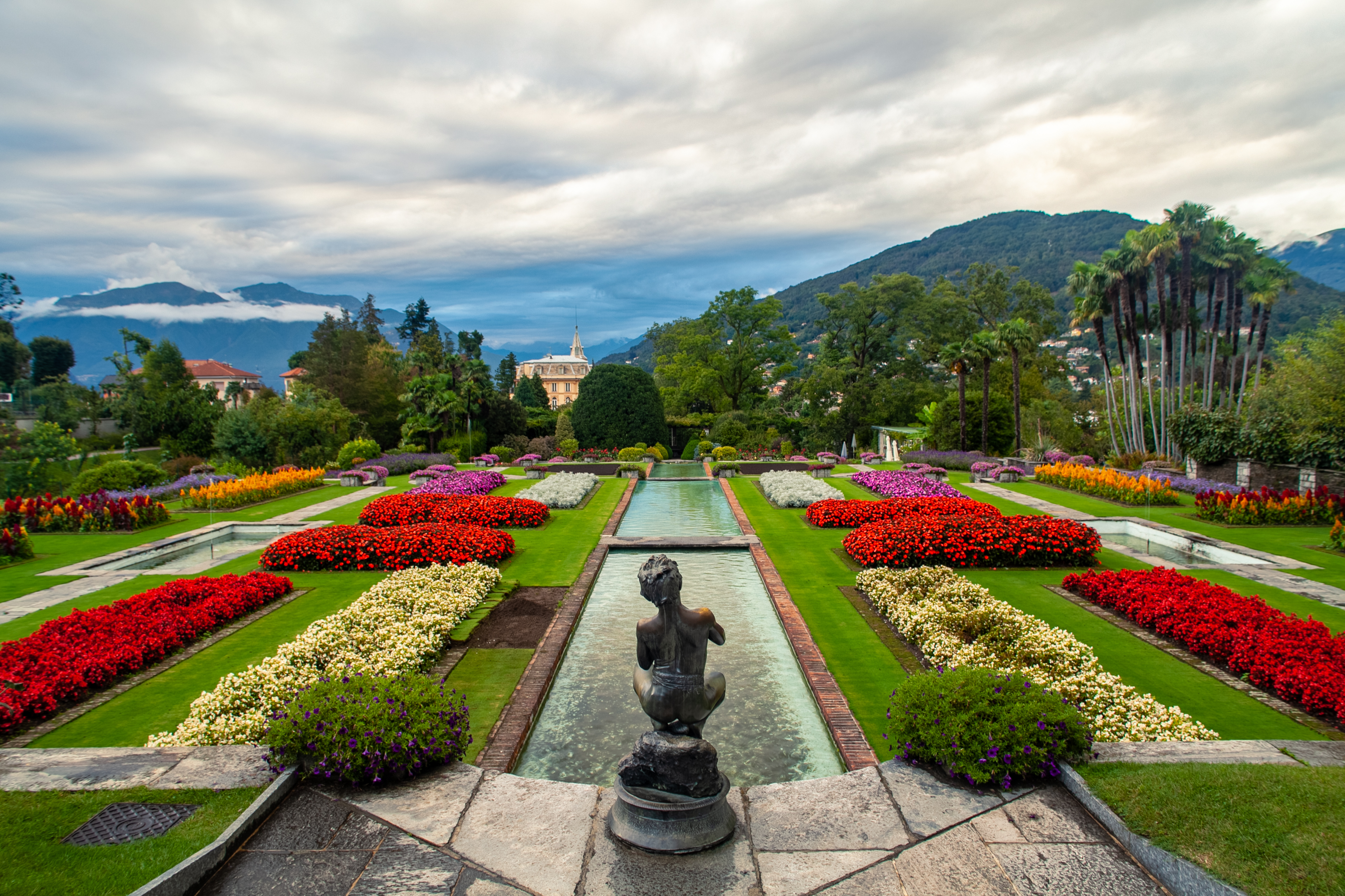Farverige blomsterbede og vandkanal i Villa Taranto botaniske have i Verbania med udsigt over Lago Maggiore og bjergene i Piemonte, Italien