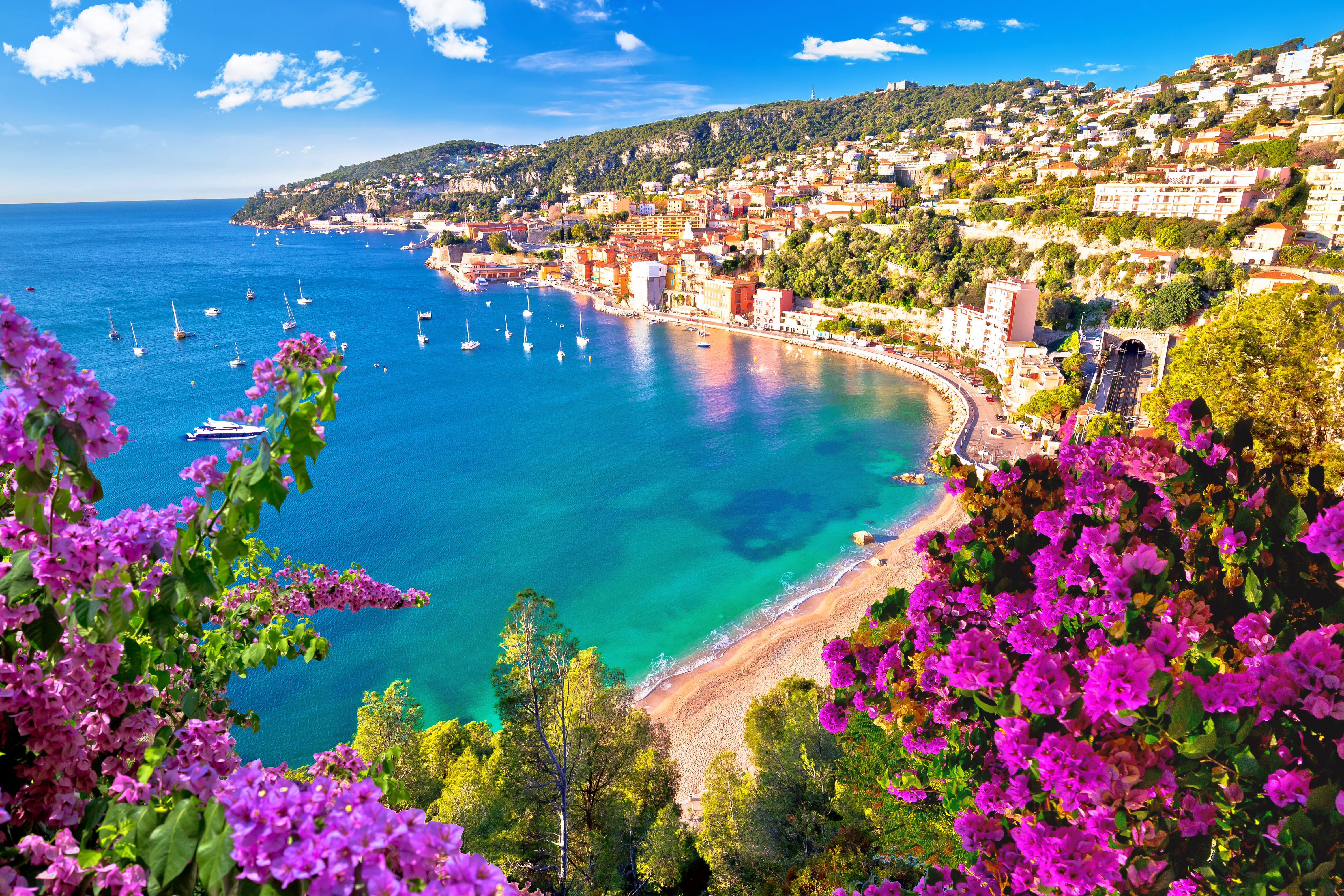 Betagende luftfoto af Villefranche-sur-Mer med dens azurblå bugt, farverige middelhavsarkitektur og sejlbåde i havnen langs den franske riviera i Alpes-Maritimes