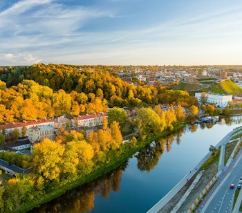Betagende luftfoto af Vilnius by i efterårsfarver med orange og gule træer ved solnedgang, der viser Litauens historiske hovedstad langs floden