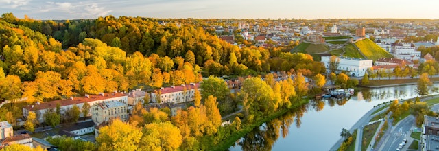 Betagende luftfoto af Vilnius by i efterårsfarver med orange og gule træer ved solnedgang, der viser Litauens historiske hovedstad langs floden