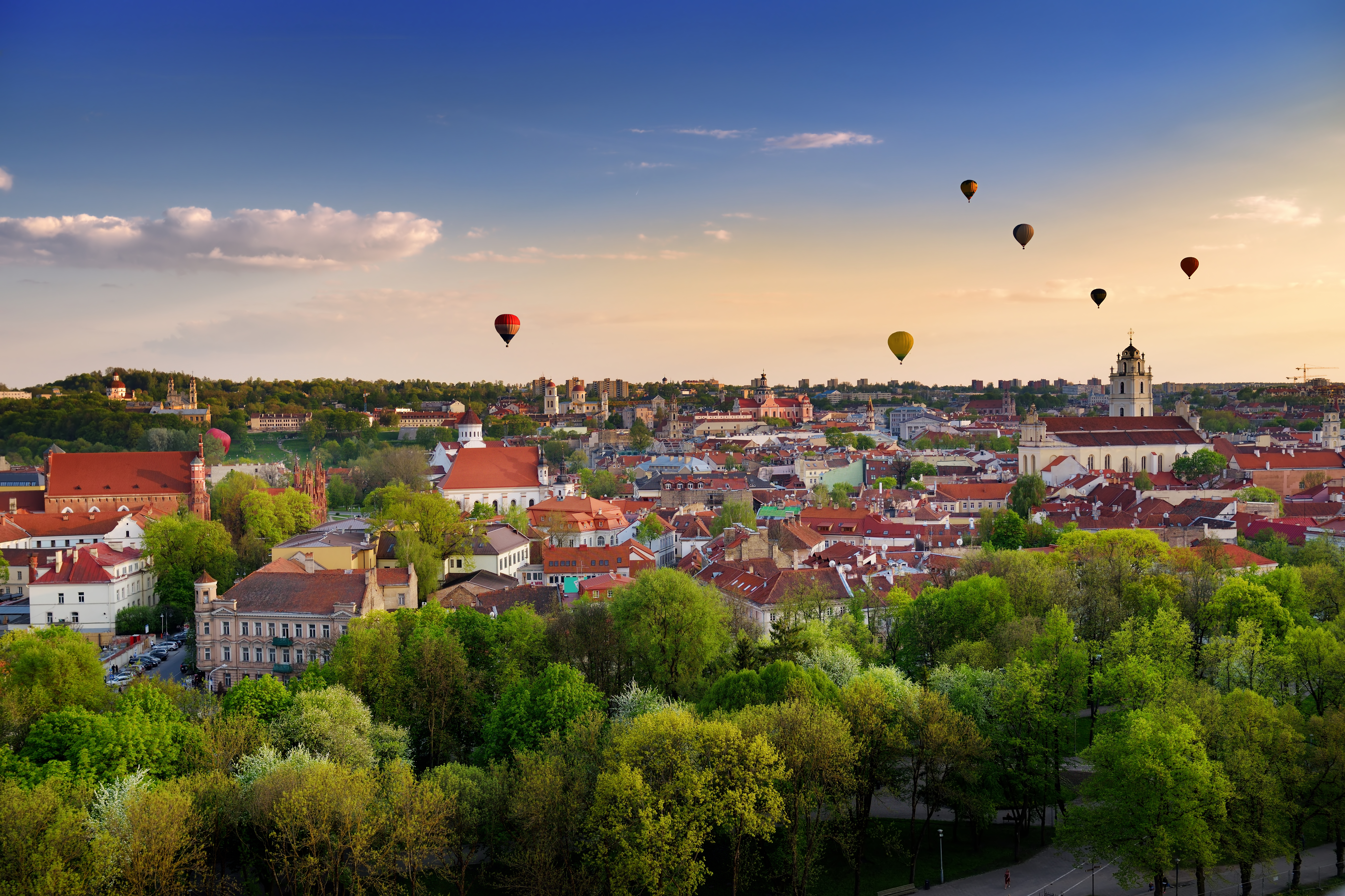 Luftballoner over Vilnius historiske bydel ved solnedgang med farverige bygninger og grønne træer