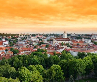 Betagende panoramaudsigt over Vilnius' gamle bydel i gyldent aftenlys, med historiske bygninger og kirketårne set fra Gediminas-højen i Litauens hovedstad