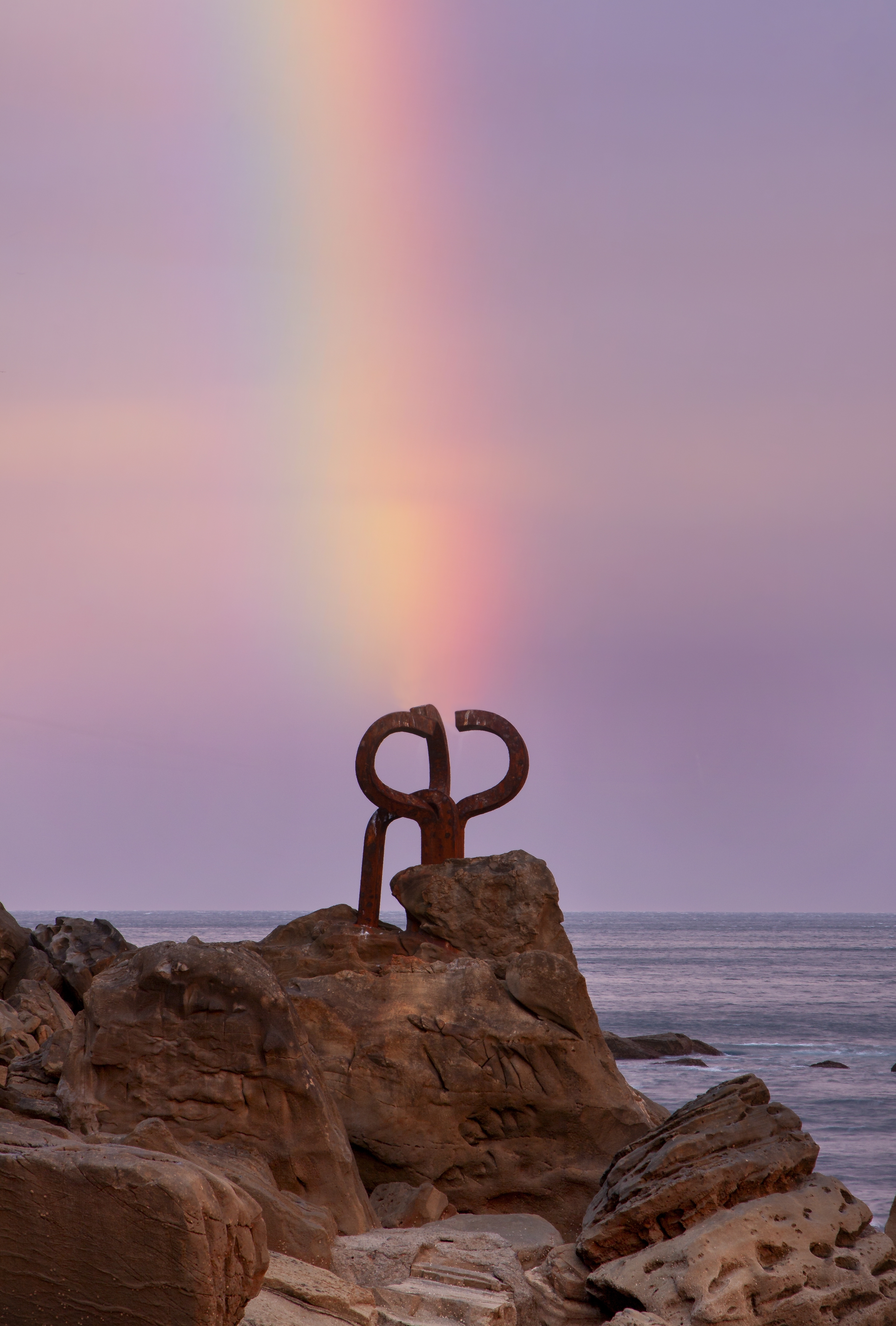 Den ikoniske skulptur Peine del Viento (Vindens kam) med regnbue ved solnedgang i San Sebastian, Baskerlandet, Spanien