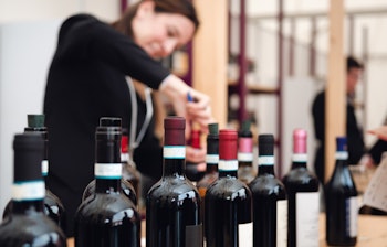 Kvindelig sommelier der åbner en flaske Dolcetto rødvin under en vinsmagningsoplevelse i Piemonte, Italien med lokale vinflasker i forgrunden