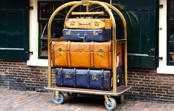 Nostalgiske læderkufferter stablet på gylden bagagevogn foran traditionel murstensbygning, symboliserer rejseminder og eventyr