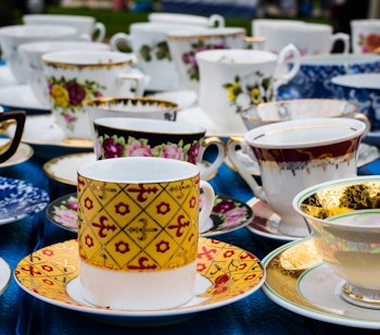 Farverige antikke tekopper og underkopper udstillet på et traditionelt loppemarked i Paris