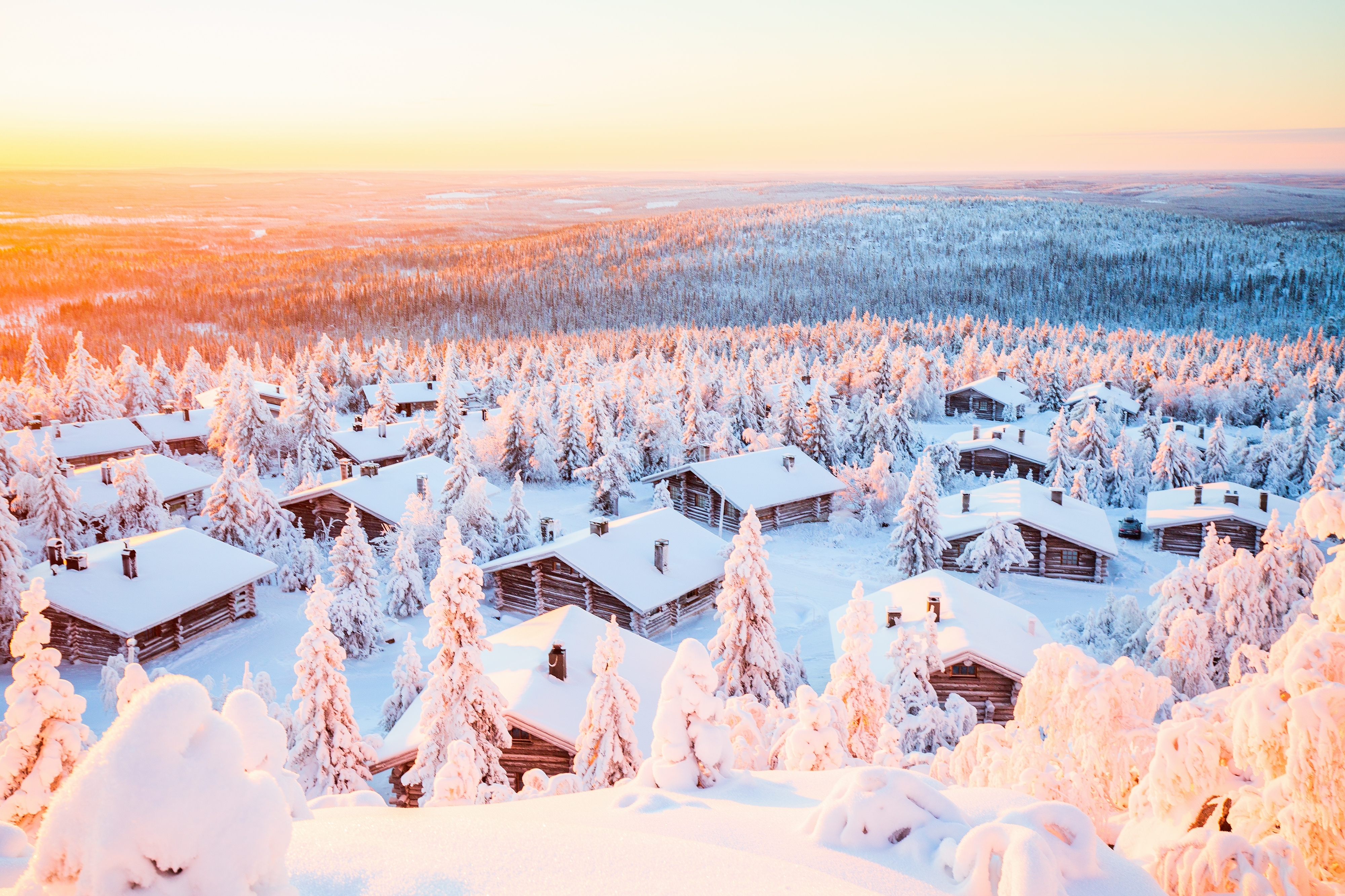 Snedækkede træhytter i finsk Lapland ved solopgang