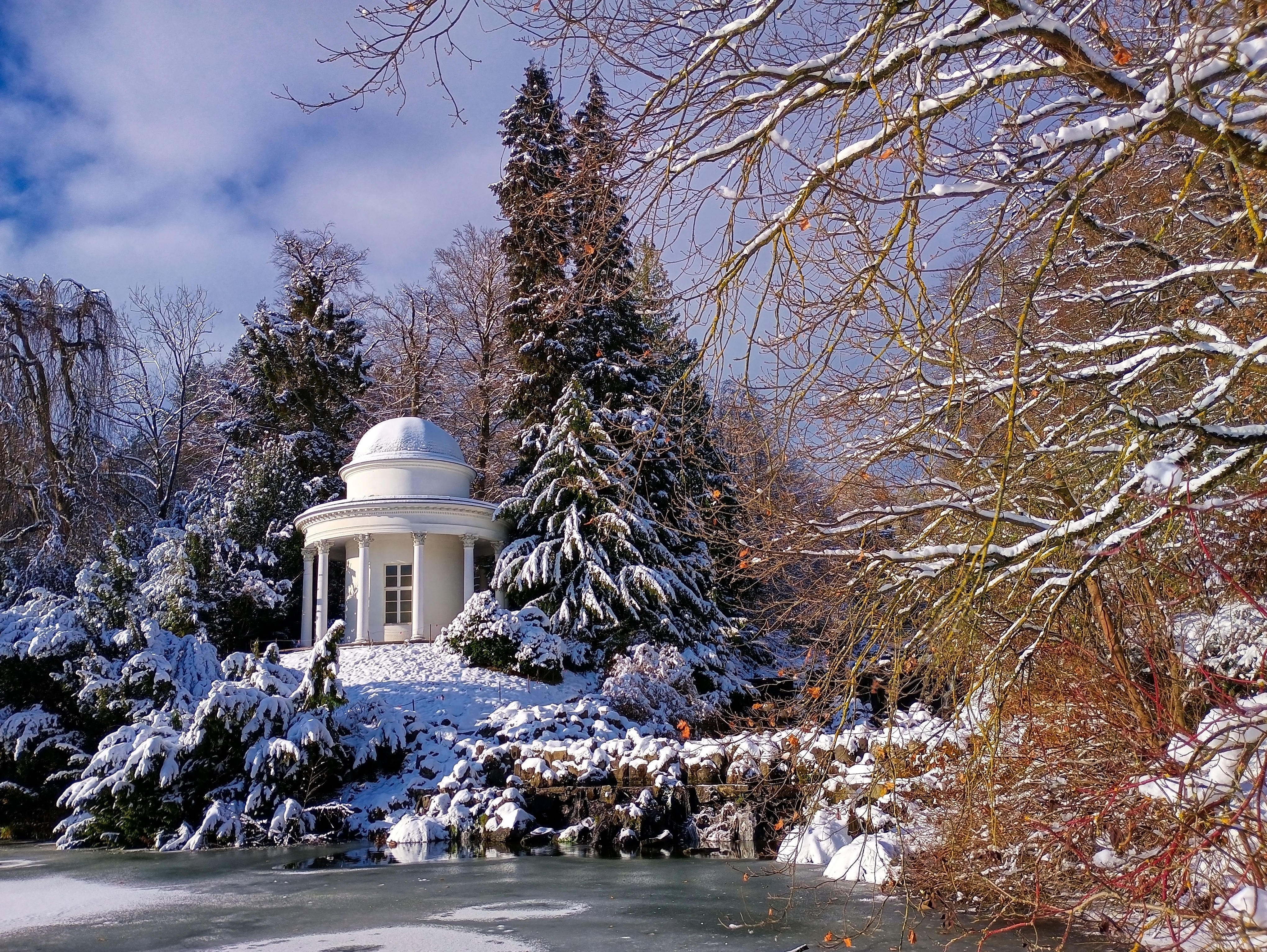 Historisk tempel i sneklædt vinterlandskab i Bergpark Wilhelmshöhe i Kassel, Tyskland med frosset vandhul og snedækkede træer