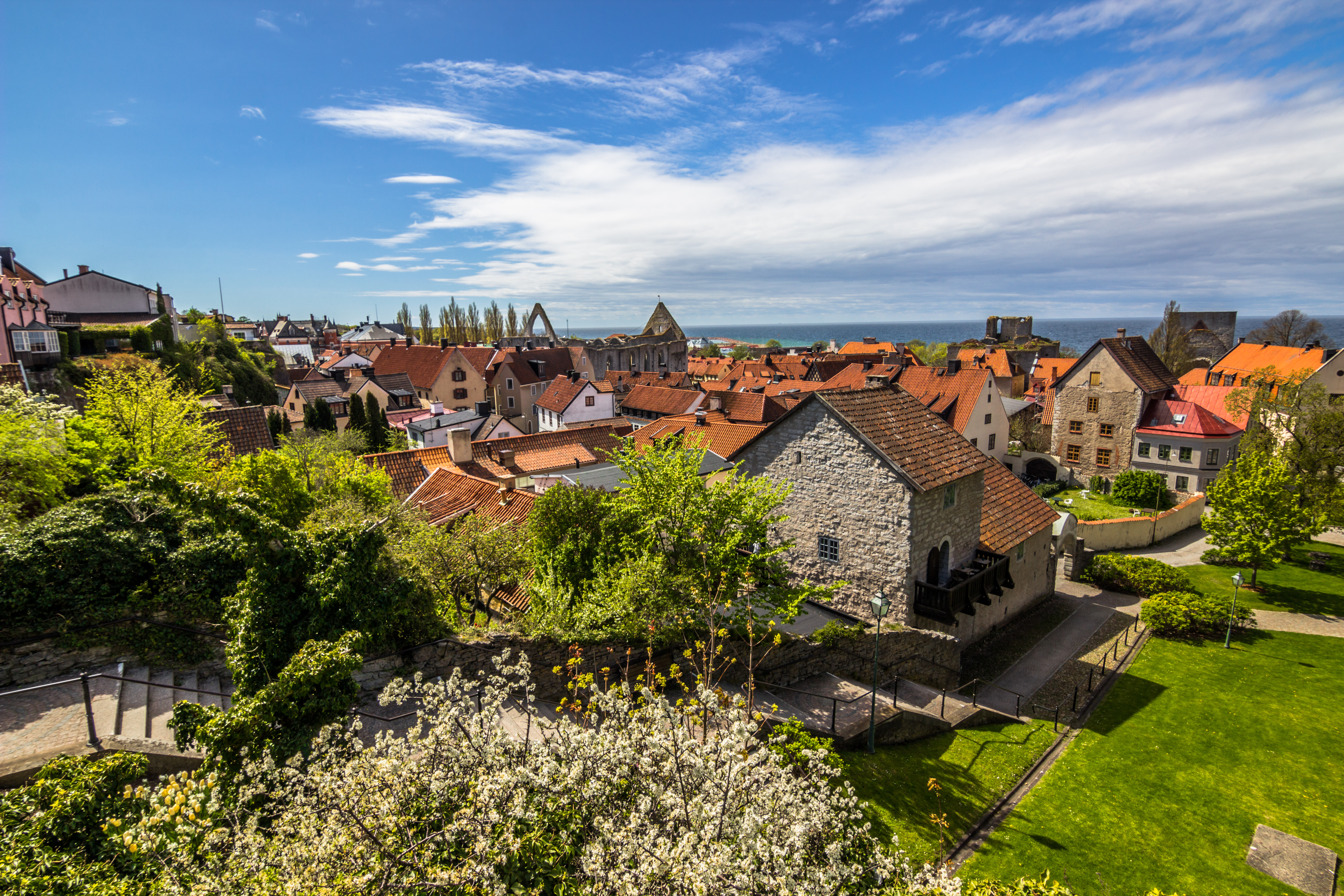 Betagende udsigt over den historiske middelalderby Visby på Gotland, Sverige, med dens velbevarede bymur, karakteristiske kirketårne og farverige huse omgivet af frodig grøn vegetation