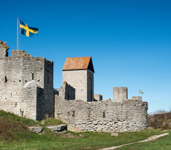Middelalderlige borgruiner med svensk flag på Gotland, historisk fæstning med stenmure og tårne