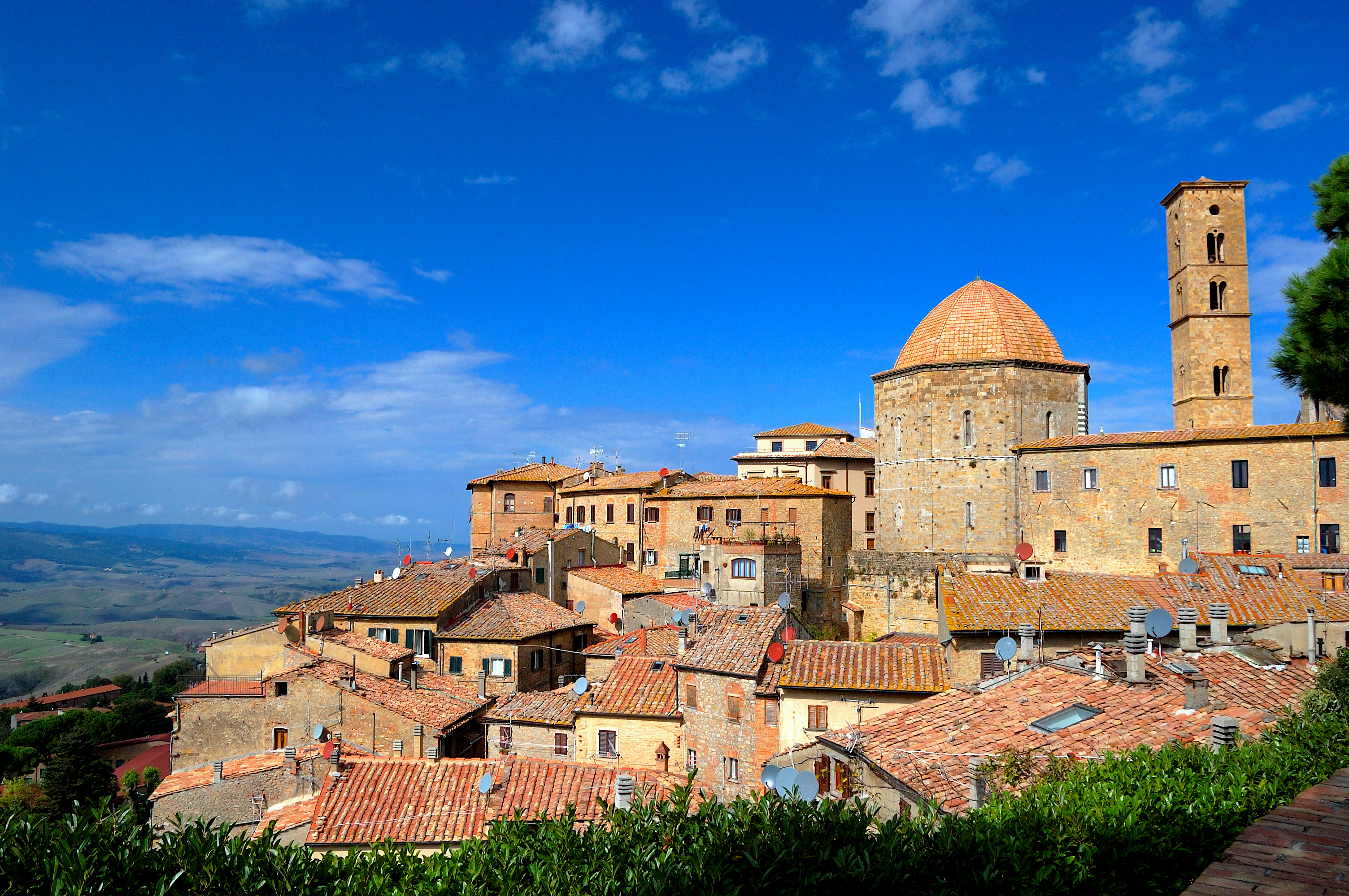 Panoramisk udsigt over den historiske middelalderby Volterra i Toscana med traditionelle stenhuse, tårne og kirker beliggende på en bakketop med det smukke toscanske landskab i baggrunden