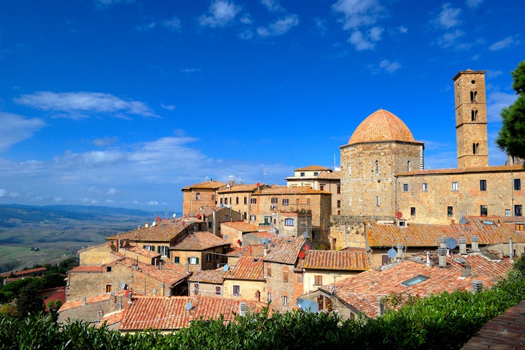 Panoramisk udsigt over den historiske middelalderby Volterra i Toscana med traditionelle stenhuse, tårne og kirker beliggende på en bakketop med det smukke toscanske landskab i baggrunden