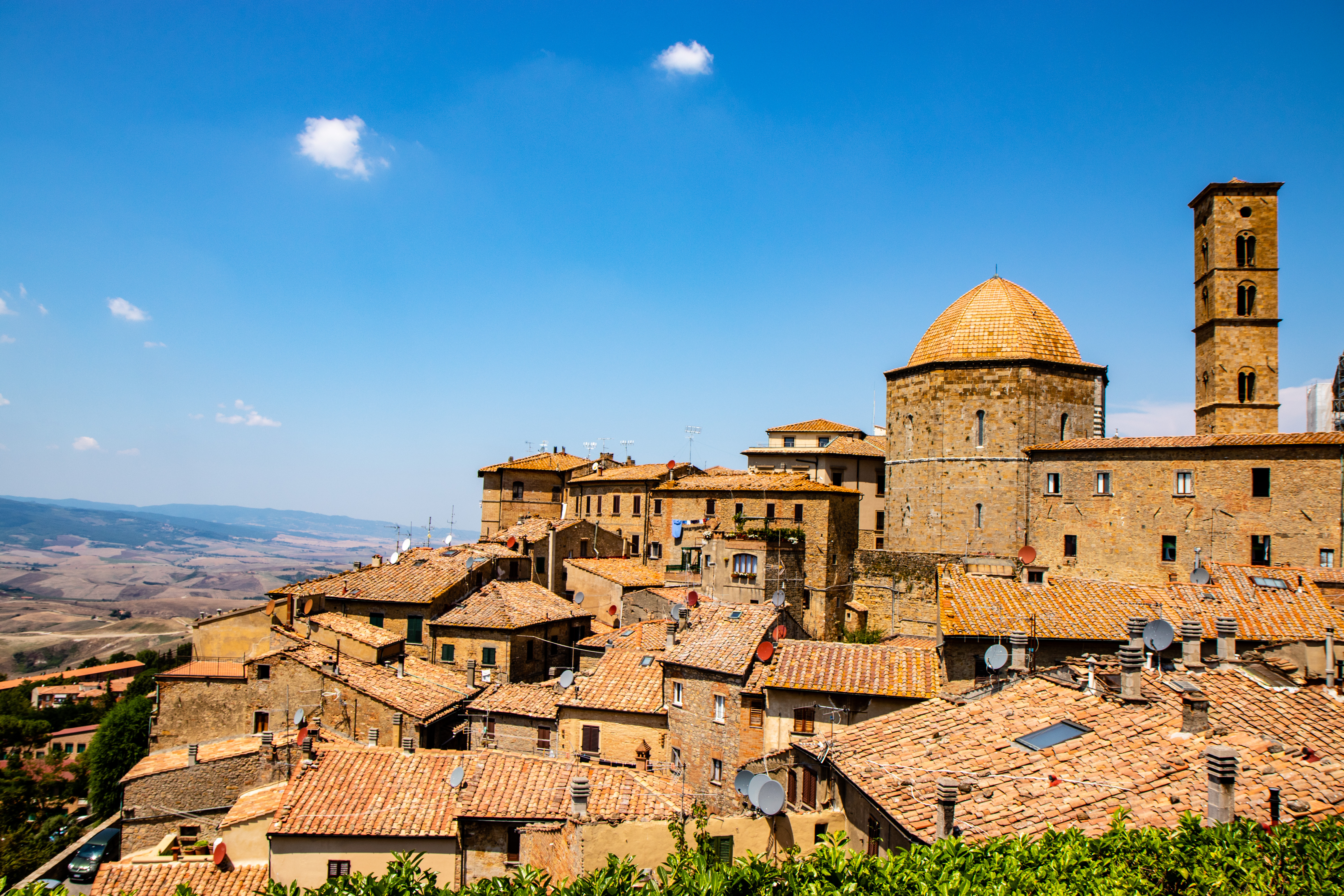 Panoramaudsigt over den middelalderlige bjergby Volterra i Toscana, Italien, med terrakottatage og historisk katedralekuppel under blå himmel