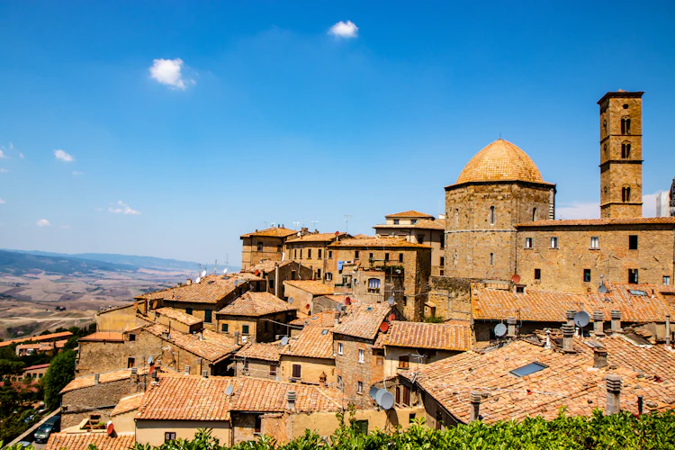 Panoramaudsigt over den middelalderlige bjergby Volterra i Toscana, Italien, med terrakottatage og historisk katedralekuppel under blå himmel