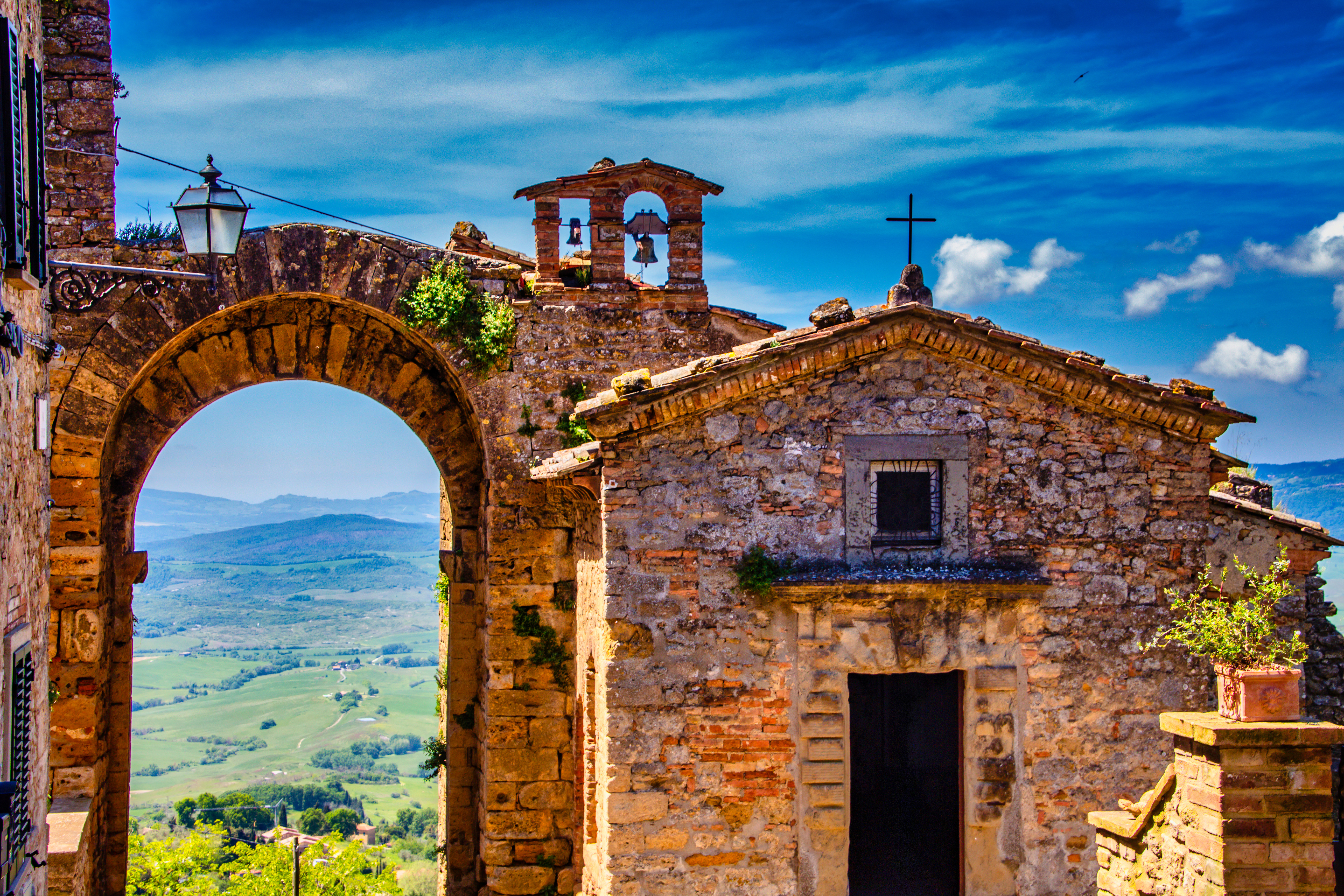 Historisk stenkirke med klokketårn og smuk bue-port i Volterra, Toscana, med udsigt over det grønne italienske landskab