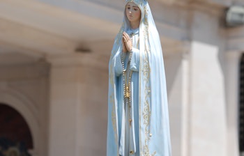 Hvid statue af Vor Frue af Fatima med krone båret i religiøs procession omgivet af hvide blomster ved helligdommen i Fatima, Portugal