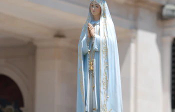 Hvid statue af Vor Frue af Fatima med krone båret i religiøs procession omgivet af hvide blomster ved helligdommen i Fatima, Portugal