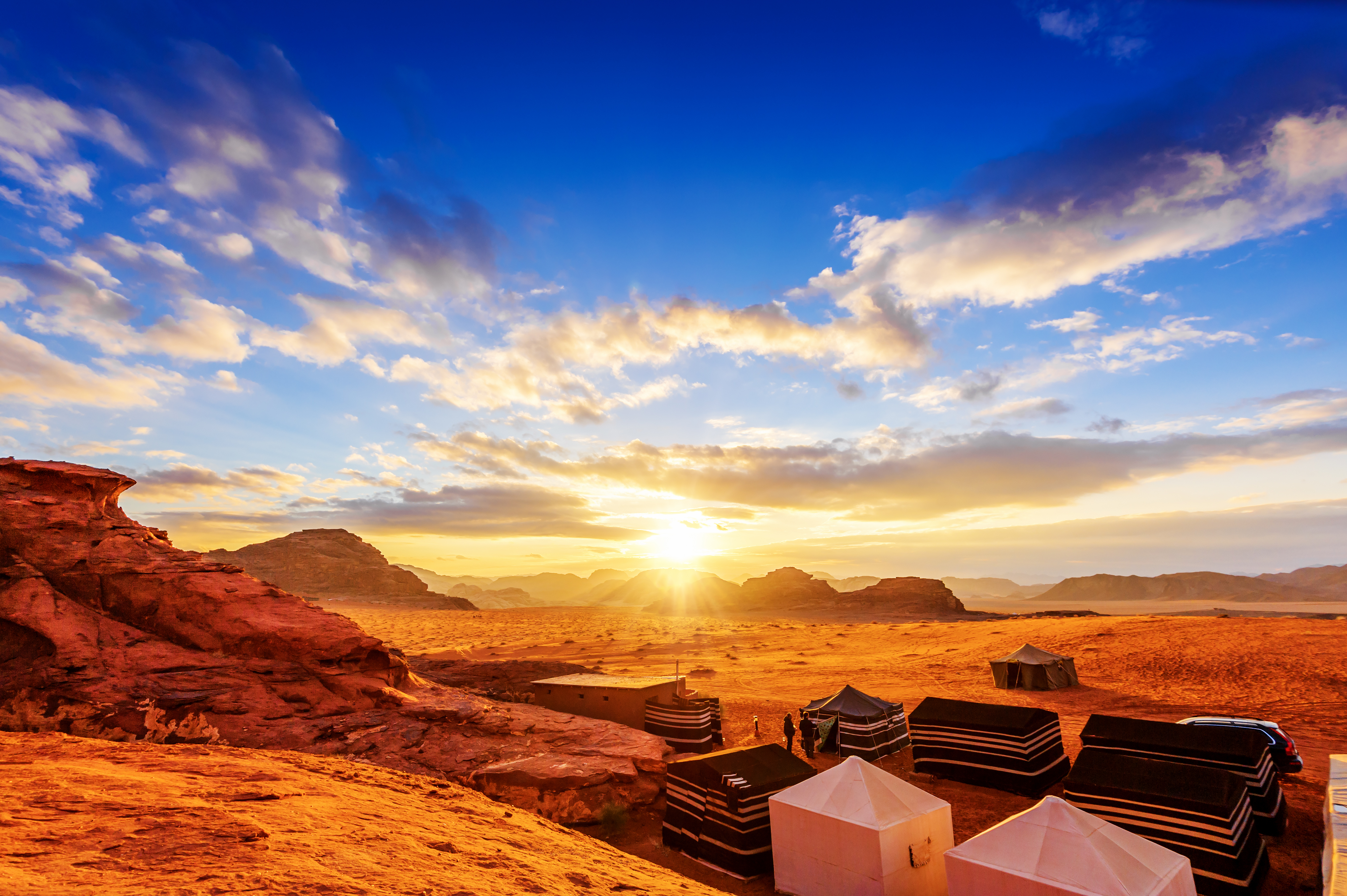 Solnedgang over Wadi Rum ørkenen i Jordan med røde sandstensformationer og beduintelte under en dramatisk himmel