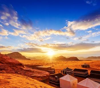Solnedgang over Wadi Rum ørkenen i Jordan med røde sandstensformationer og beduintelte under en dramatisk himmel