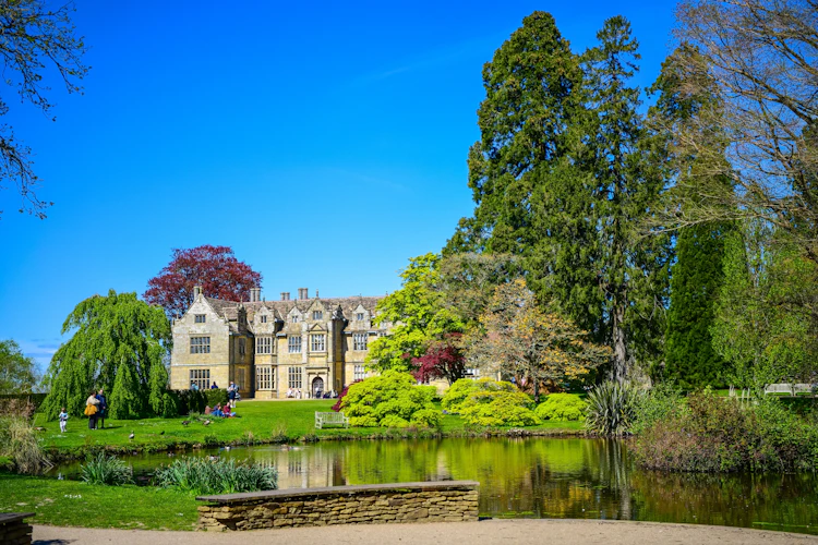 Historisk Wakehurst Place herregård spejlet i en fredfyldt havesø omgivet af frodig forårsgrønt i West Sussex, England