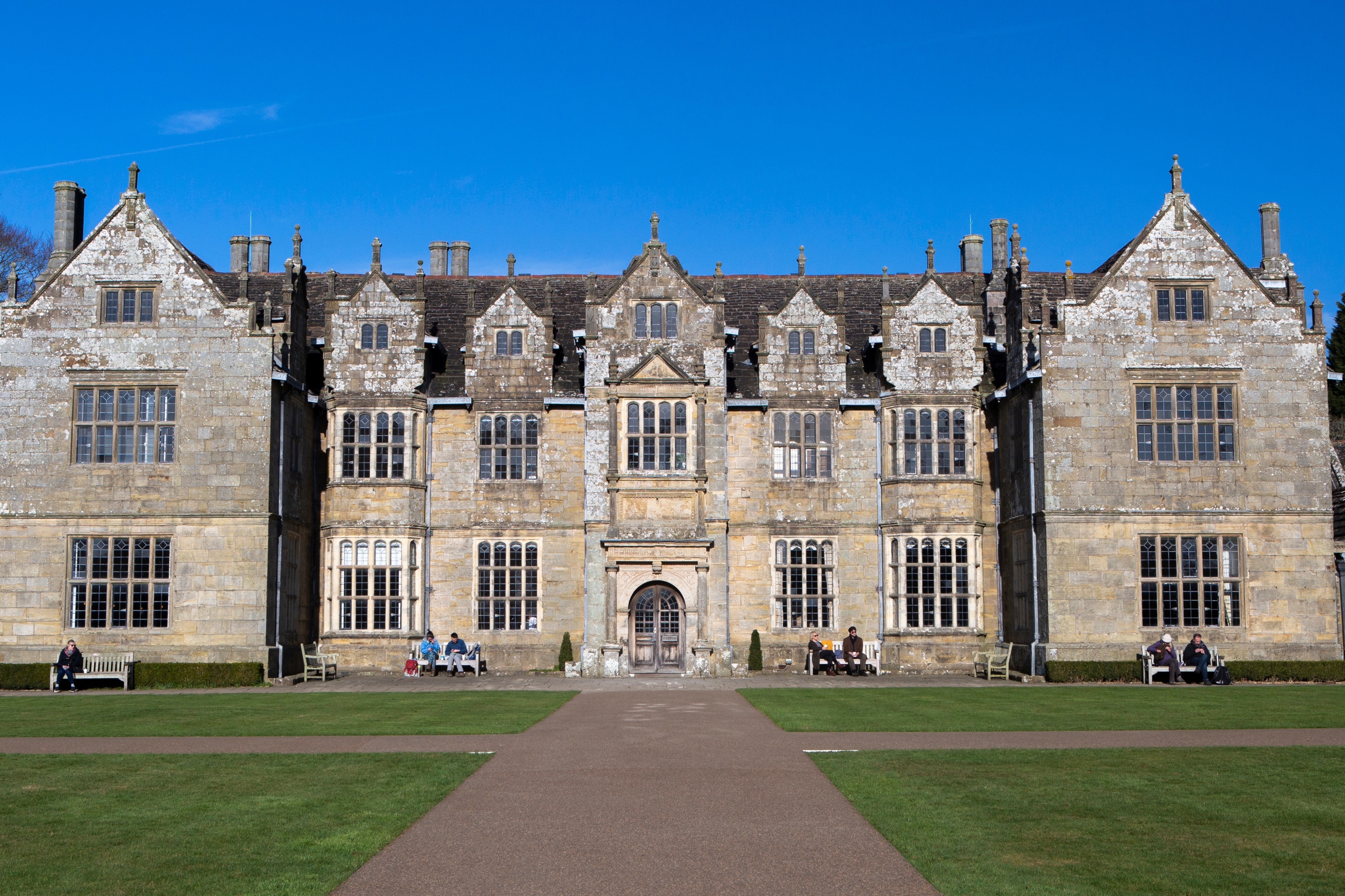 Wakehurst Place historisk herregård i West Sussex, England, omgivet af velplejet græsplæne og blå himmel