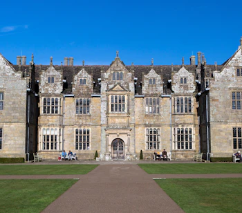Wakehurst Place historisk herregård i West Sussex, England, omgivet af velplejet græsplæne og blå himmel