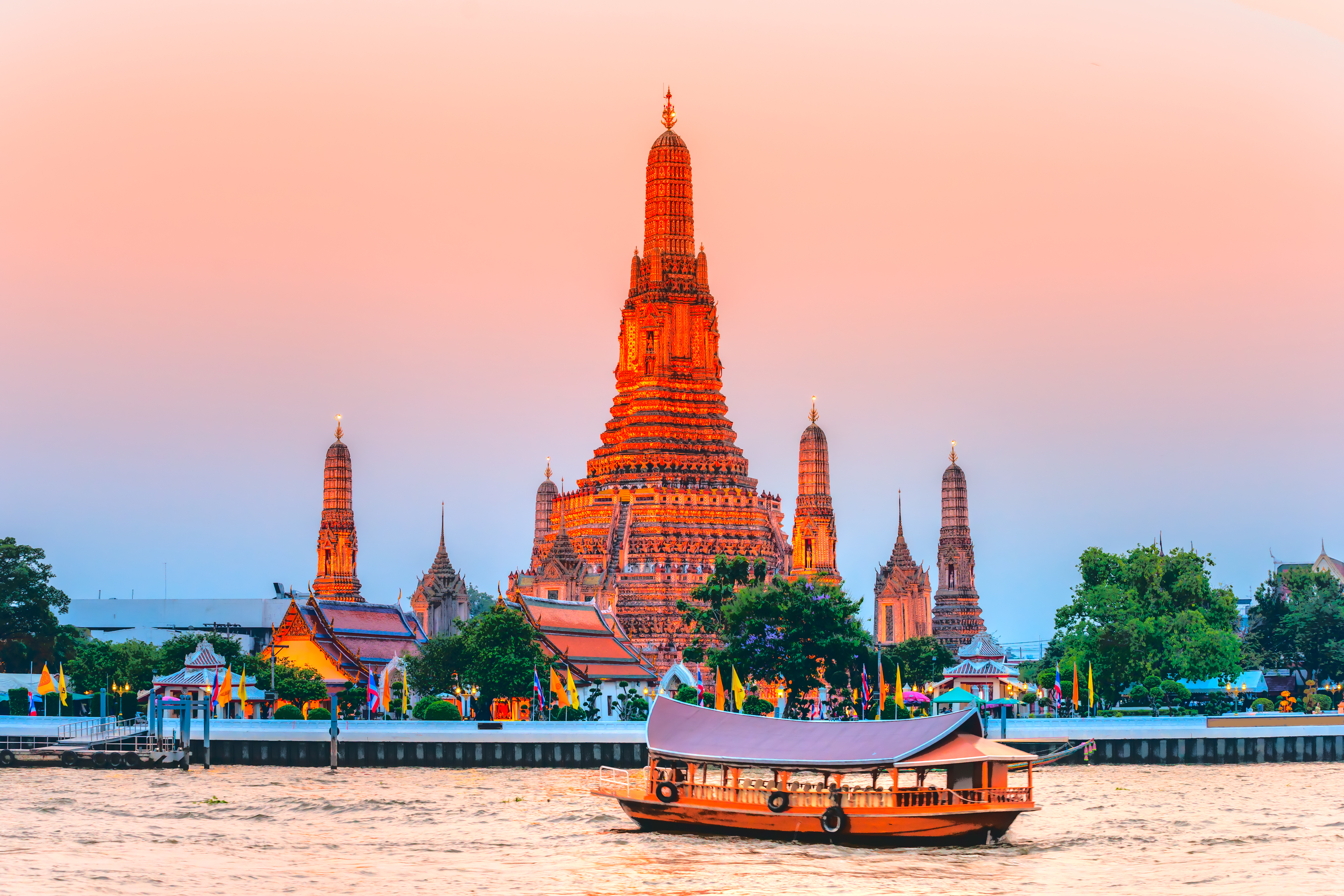 Wat Arun tempel i Bangkok ved solnedgang med traditionel baad paa Chao Phraya floden Thailand