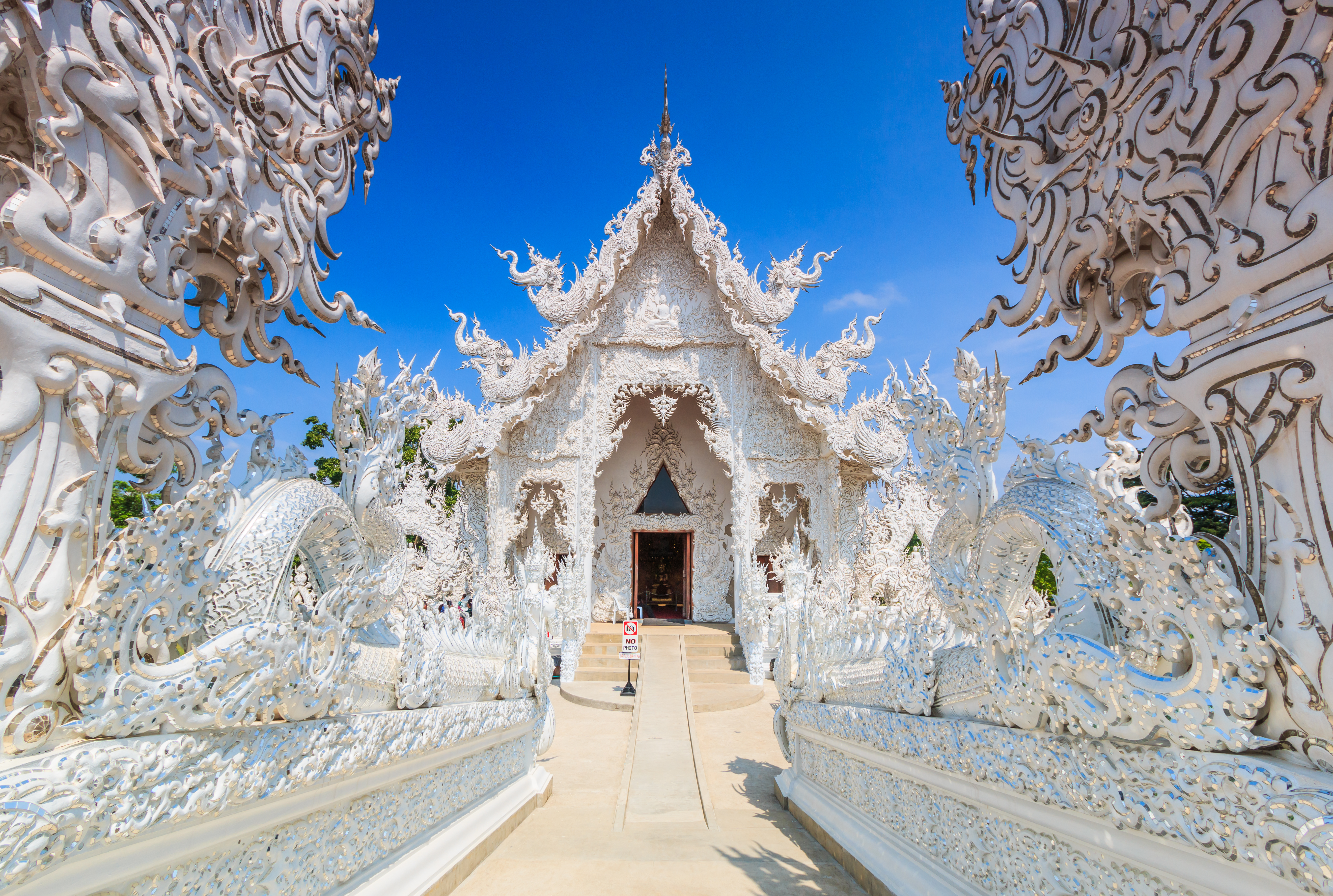 Det smukke hvide tempel Wat Rong Khun i Chiang Rai, Thailand, med detaljerede hvide udskæringer og ornamenter mod en klar blå himmel