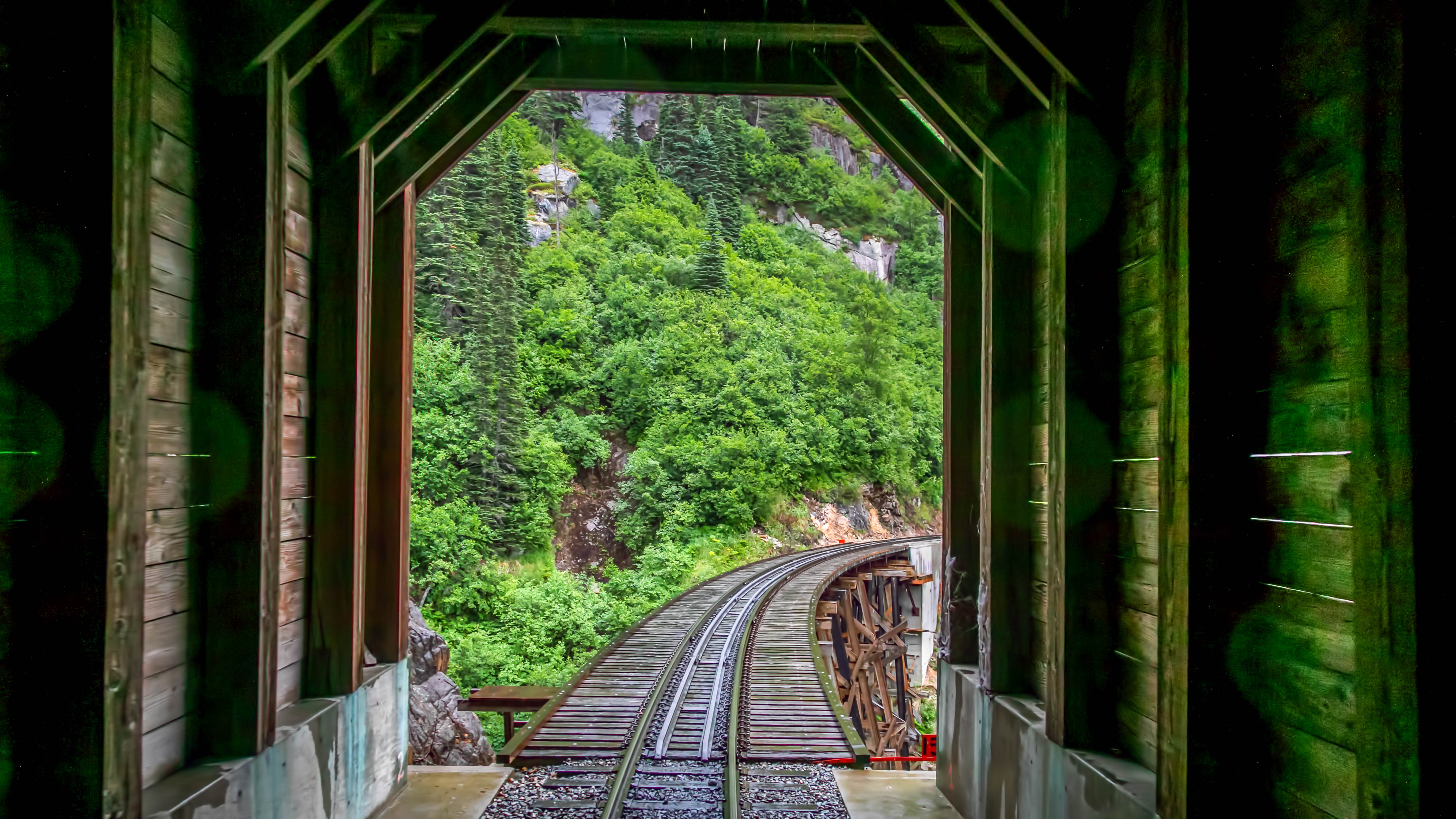 Historisk jernbanespor gennem træbro på White Pass jernbanen i Skagway, Alaska med frodigt grønt bjerglandskab