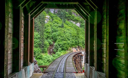 Historisk jernbanespor gennem træbro på White Pass jernbanen i Skagway, Alaska med frodigt grønt bjerglandskab