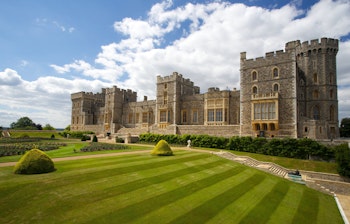 Det historiske Windsor Slot med velholdte haver og stribet græsplæne under blå himmel, kongelig residens nær London, England