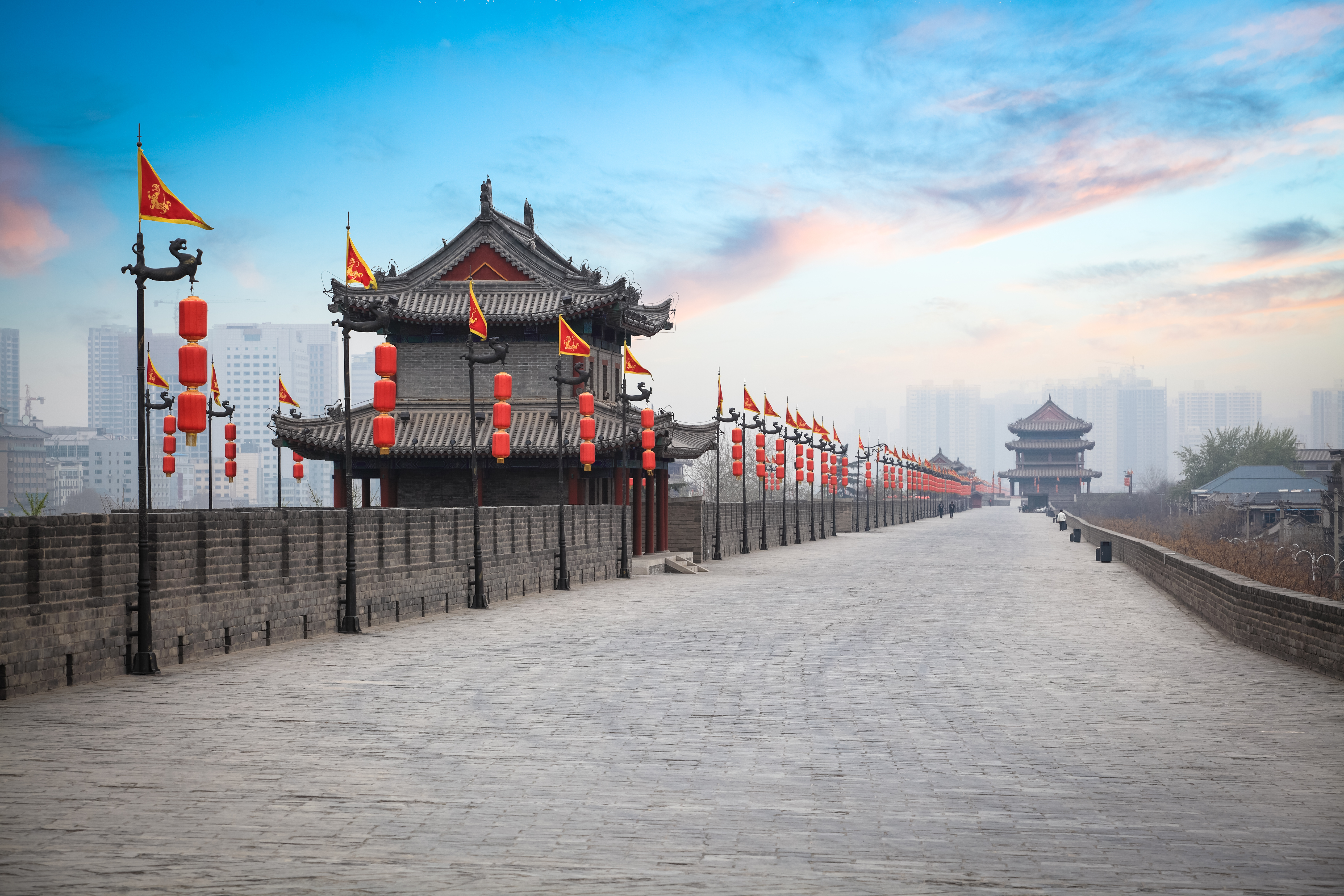 Gammel kinesisk bymur ved solnedgang med traditionelt vagttaarn og roede lygter i Xi'an