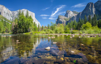 Krystalklart bjergvand med refleksioner af imponerende granitfald og grøn skov i Yosemite nationalpark