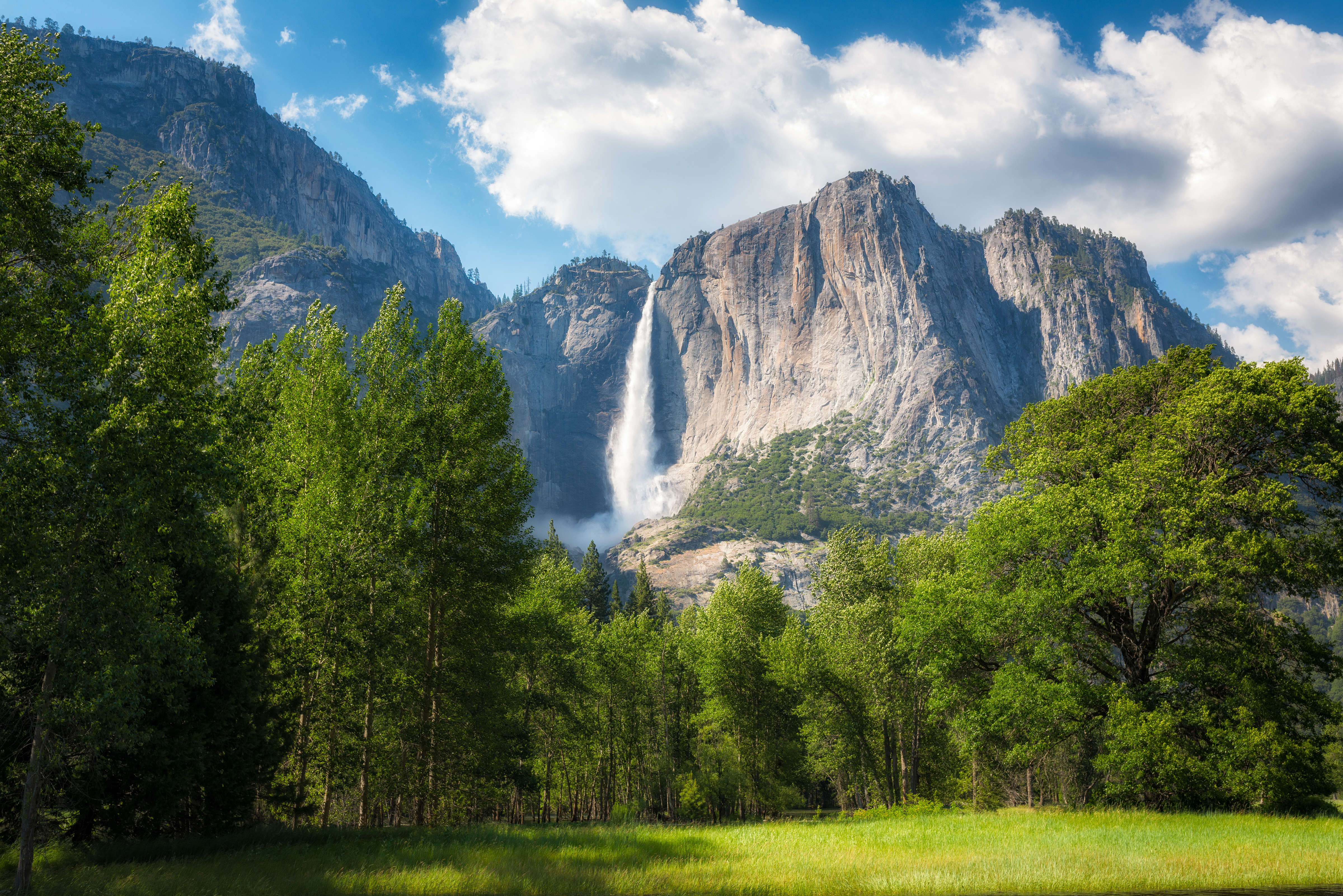 Majestaetisk Yosemite Falls med hoeje klippevægge og groen eng i forgrunden under dramatisk himmel i Californien