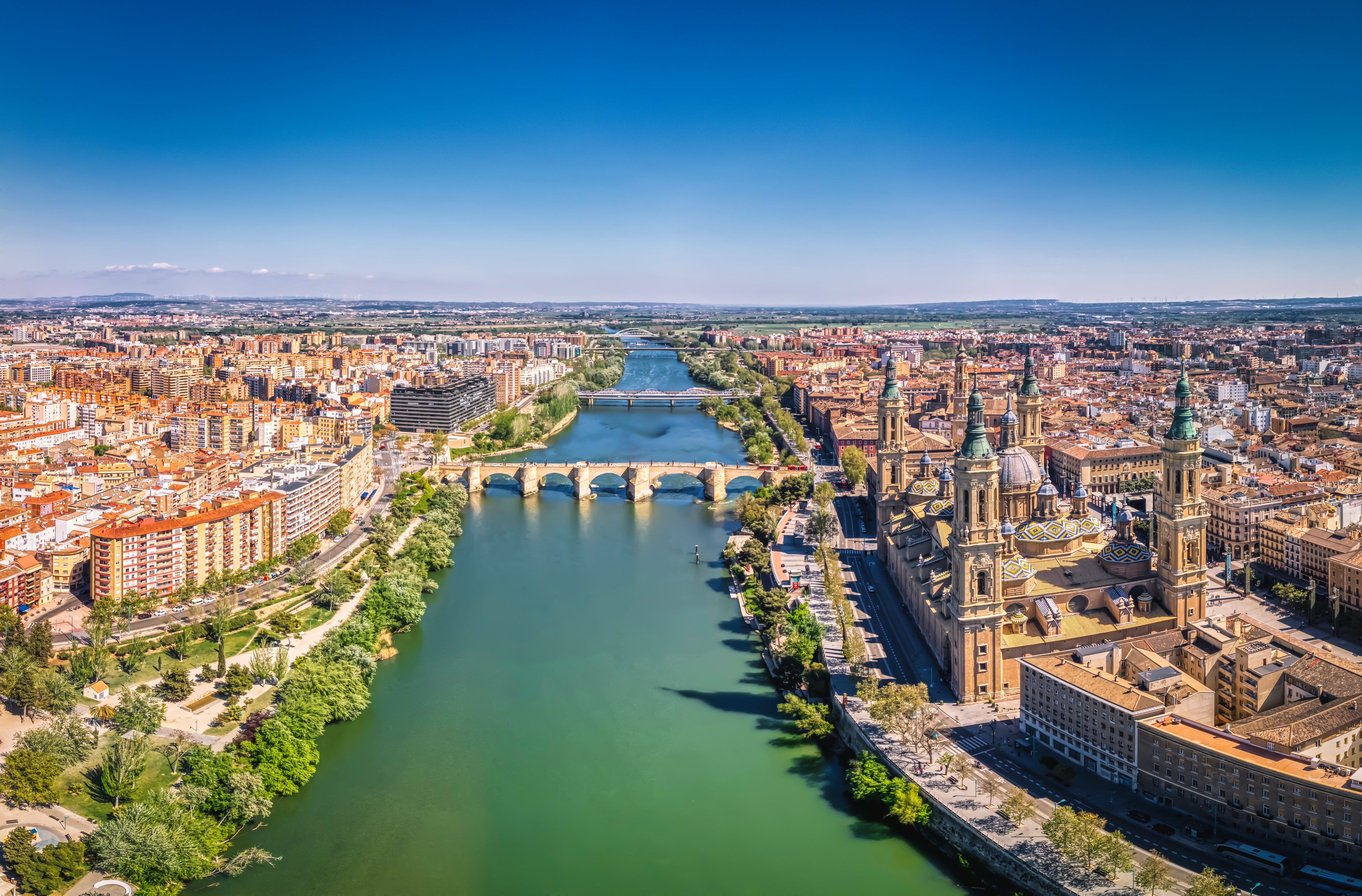 Betagende panoramaudsigt over Zaragoza med Ebro-floden, der snor sig gennem byen, og den majestætiske Basilica del Pilar, der rejser sig mod den klare blå himmel
